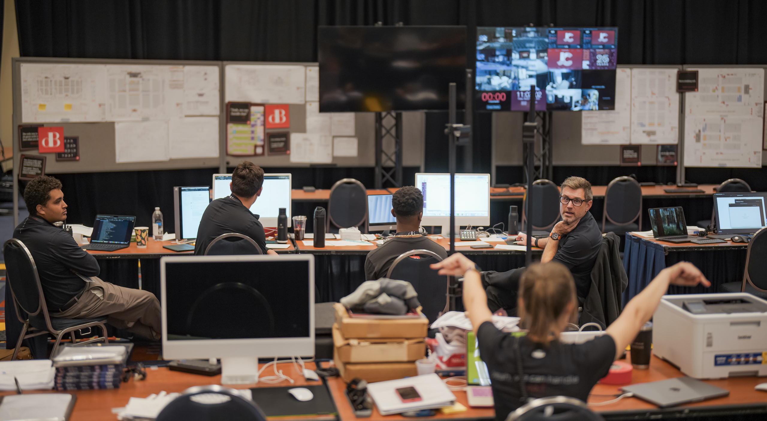 Professional corporate event producers sitting in a command center with broadcast screens and CAD drawings in an operations center for a large scale event.
