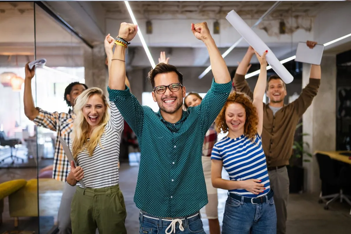 Excited employees cheering with arms raised in a modern office celebrating one of the best company event ideas for employees