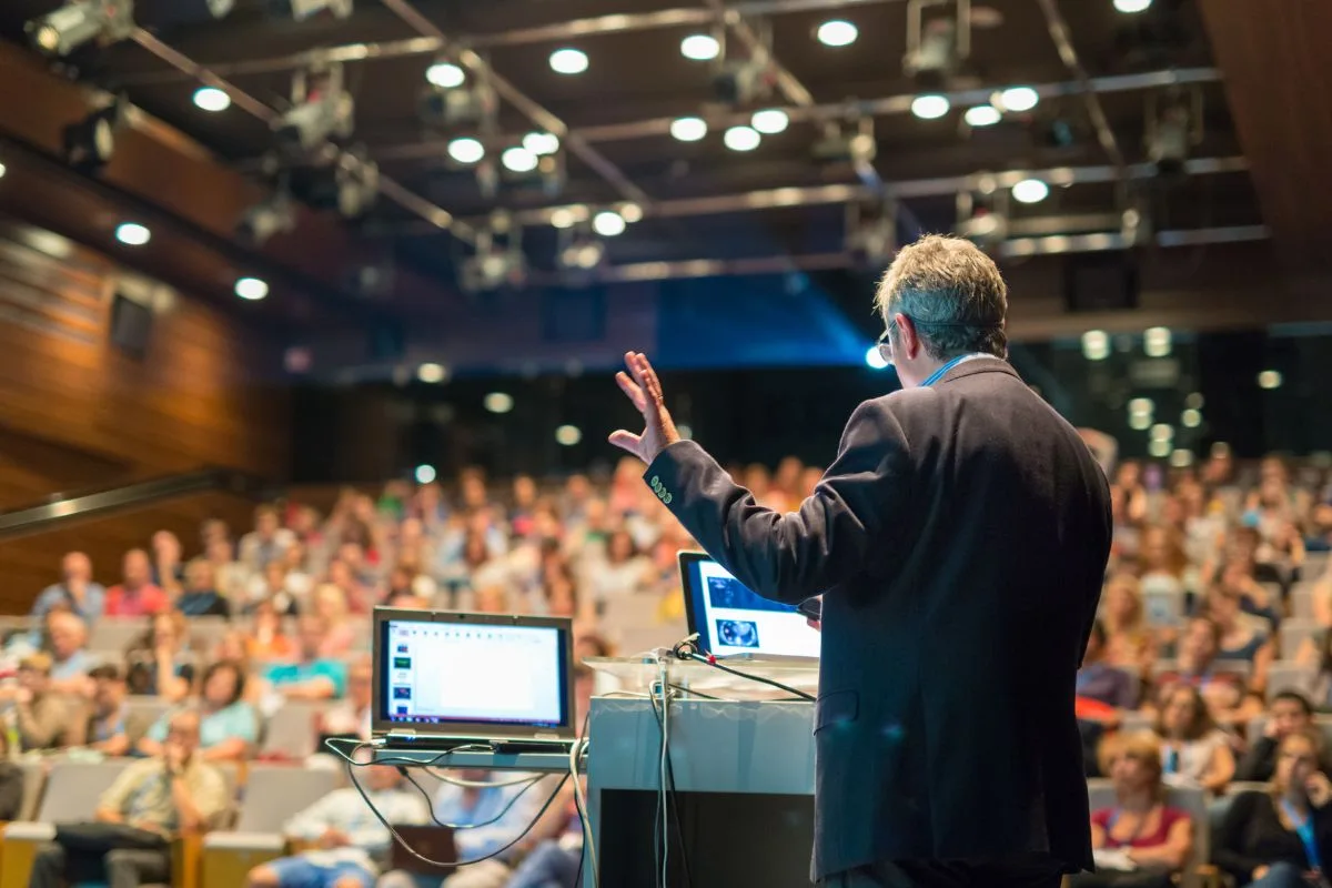 Hybrid event planning: speaker presenting to large in-person conference audience